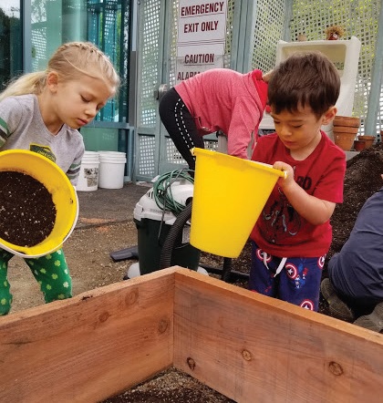 Children help fill the raised garden bed.