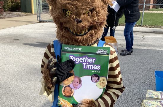 A child in a bear costume holds a Lions Quest workbook