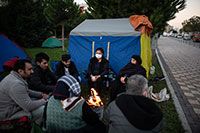 A group of people sit around a fire beside a tent.