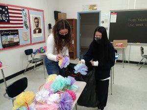 Two women sort through paper flowers. 
