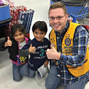 Lions Club. member giving thumbs up with two kids