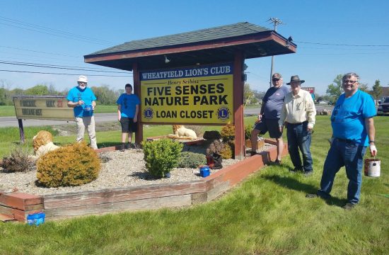 Lions club members stand in ffront of newly repainted sign