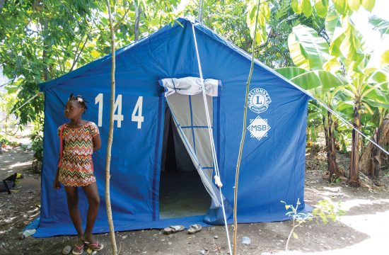 Girl stands in front of relief tent