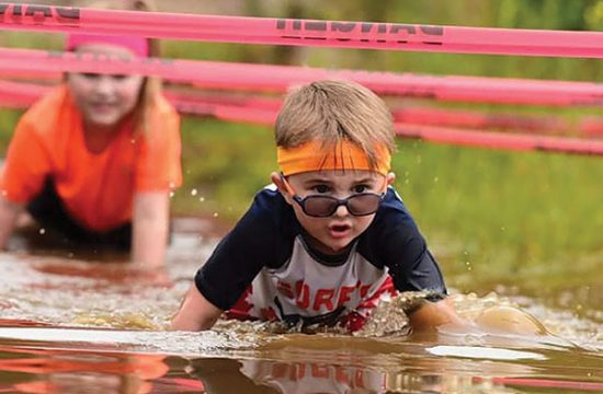 Child ducks under obstacle at mud run