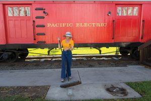 Seal Beach Lions Club member sweeps area in front of historic red car.